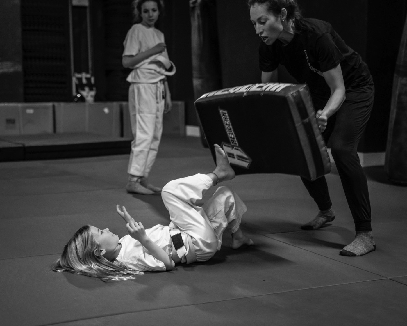 A young student kicking a pad from the ground in a Combat Club class